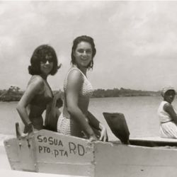 Posing for a beach photo beach visitors sit atop a wooden dinghy on the beach